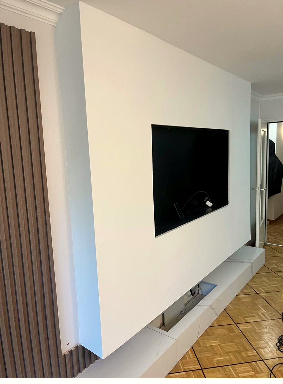 Mur TV sur mesure peint en blanc avec habillage en tasseaux de bois, réalisation JOAO DECO à Genève